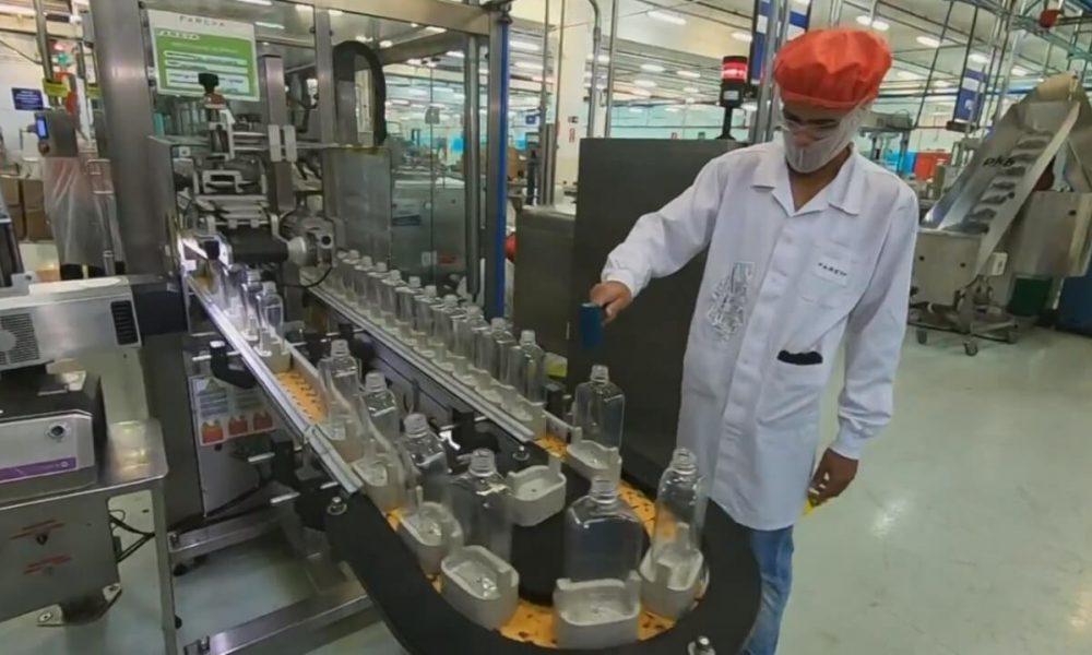 Colaborador inspeciona máquina que envasa álcool em gel