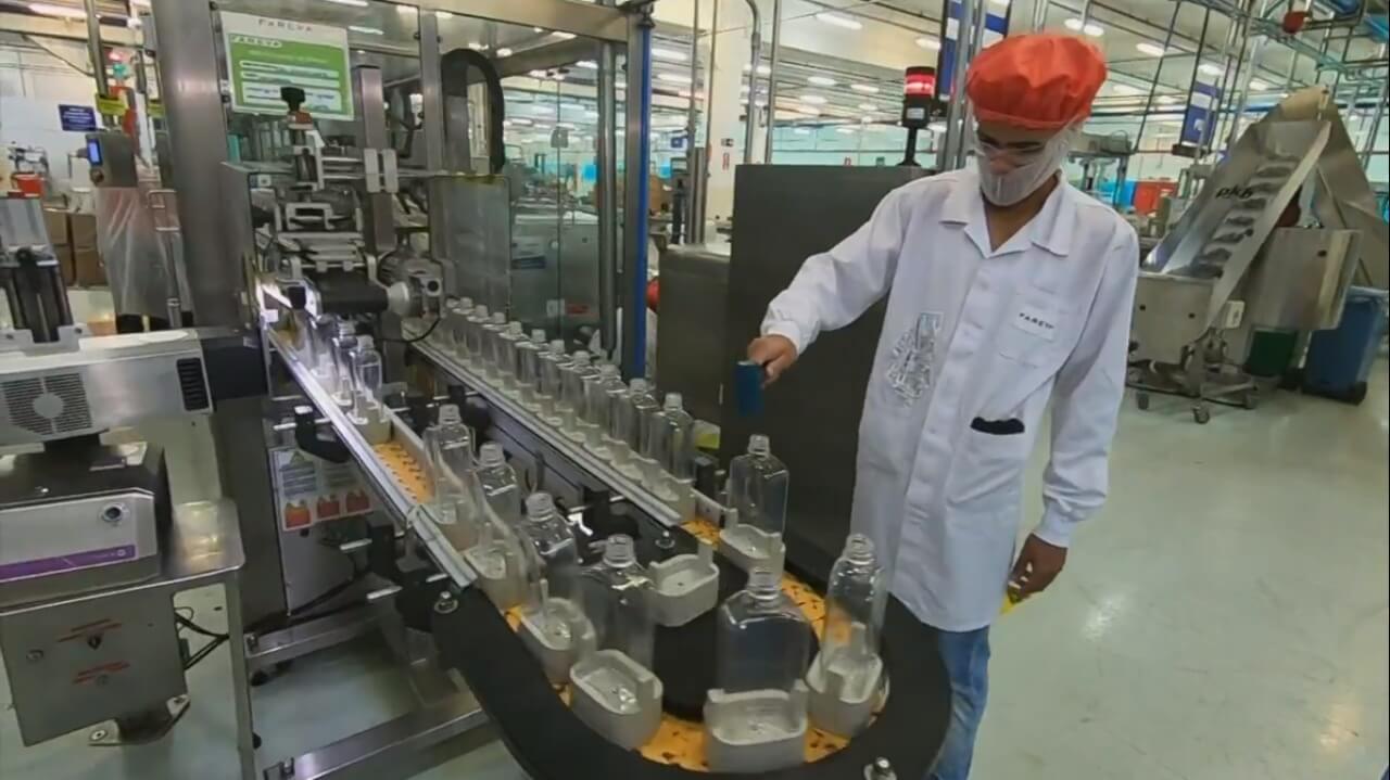 Colaborador inspeciona máquina que envasa álcool em gel