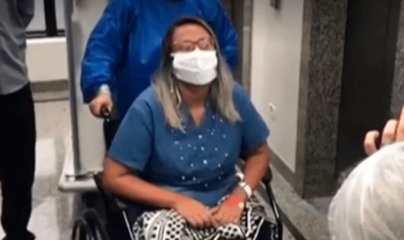Foto da paciente saindo do hospital com máscara e na cadeira de rodas