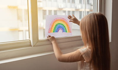 Criança cola desenho de arco-íris na janela