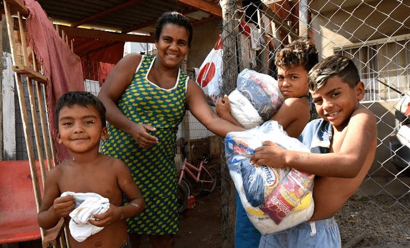 Mãe e três filhos seguram cestas básicas em frente a sua casa