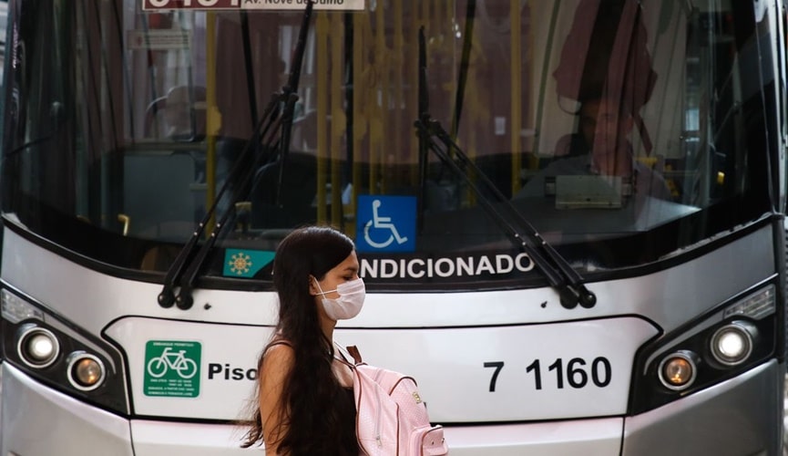 Foto de mulher atravessando de máscara na frente de ônibus
