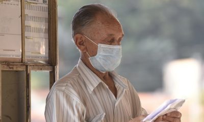Foto de idoso de máscara segurando objetos em terminal de ônibus