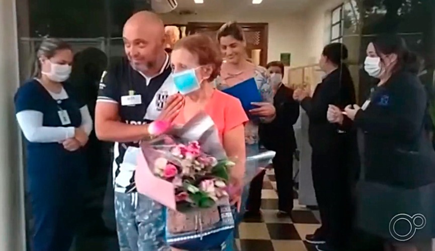 Foto de idosa com buquê de flores na saída de hospital