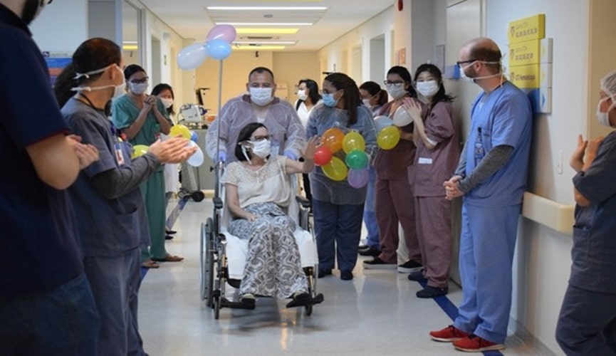 Foto de mulher em cadeira de rodas, deixando hospital com bela homenagem de enfermeiros