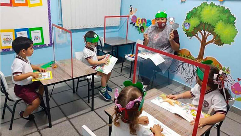 Crianças em sala de aula separadas por barreira de acrílico