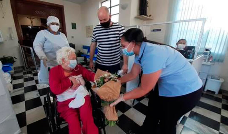 Mulher de cabelos brancos deixando hospital em cadeira de rodas