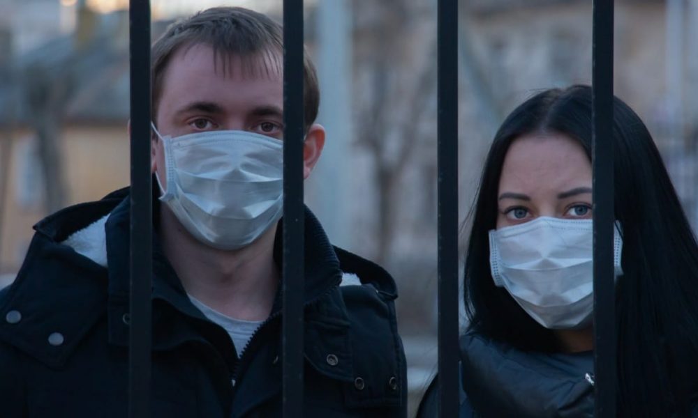 Homem e mulher usando máscara atrás de um portão