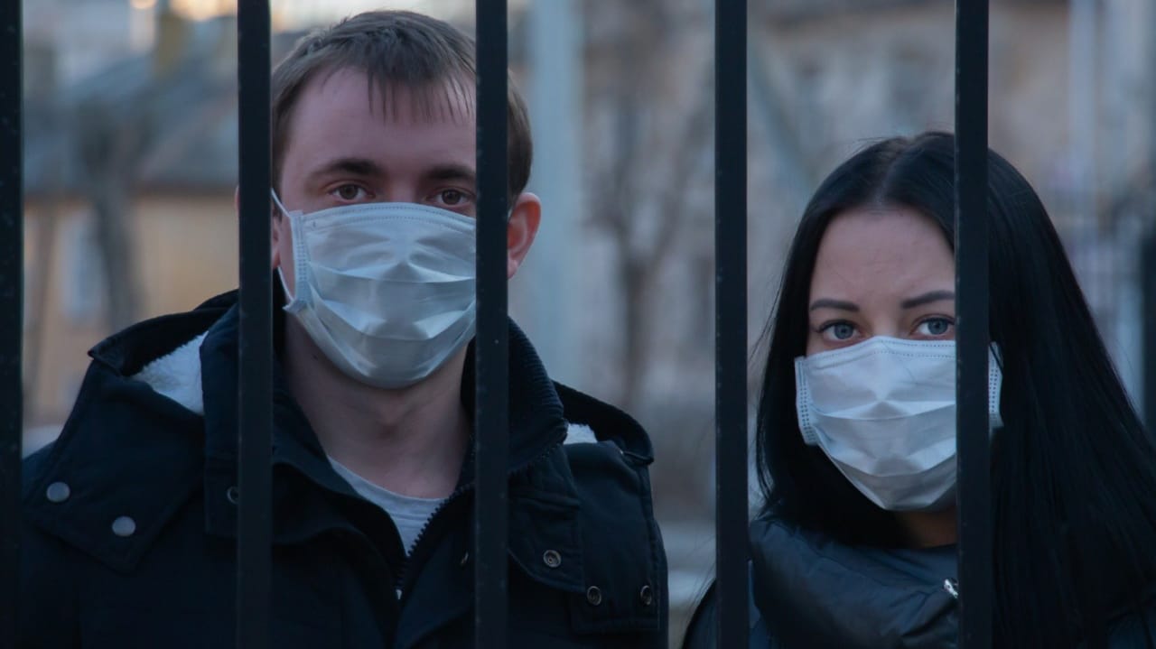Homem e mulher usando máscara atrás de um portão