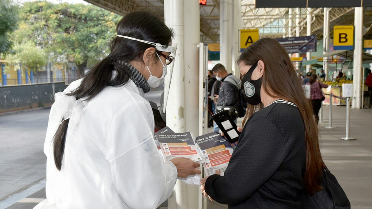 Profissional da Saúde mostrando folheto para passageira no Terminal Central