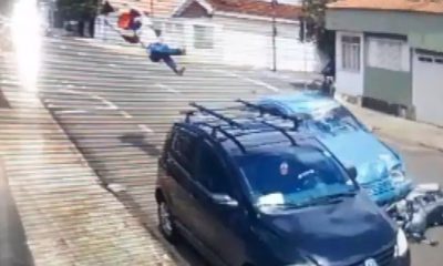 Frame de vídeo de segurança de entregador sendo arremessado após colisão com carro.
