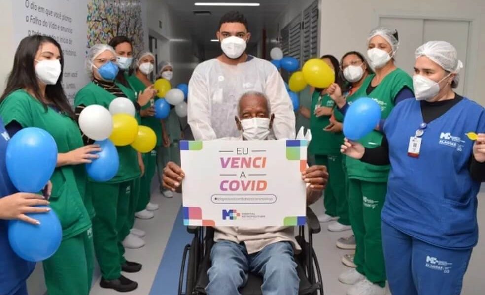 Idoso sai de hospital em cadeira de rodas com equipe médica comemorando com balões coloridos