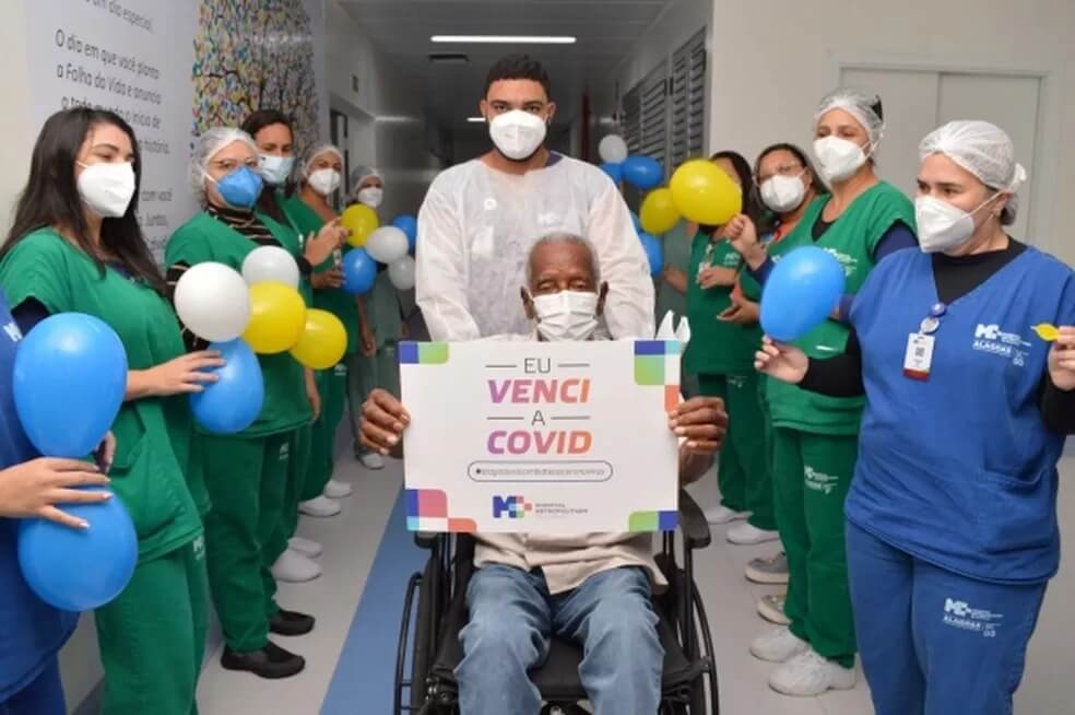 Idoso sai de hospital em cadeira de rodas com equipe médica comemorando com balões coloridos