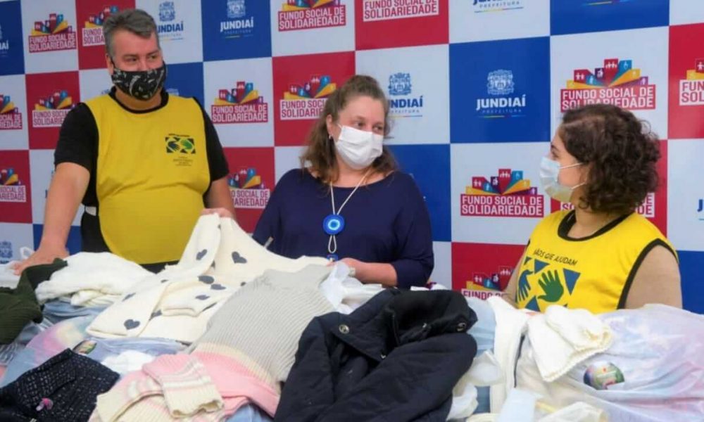 Um homem e duas mulheres em frente à doações de roupas do Fundo Social de Jundiaí