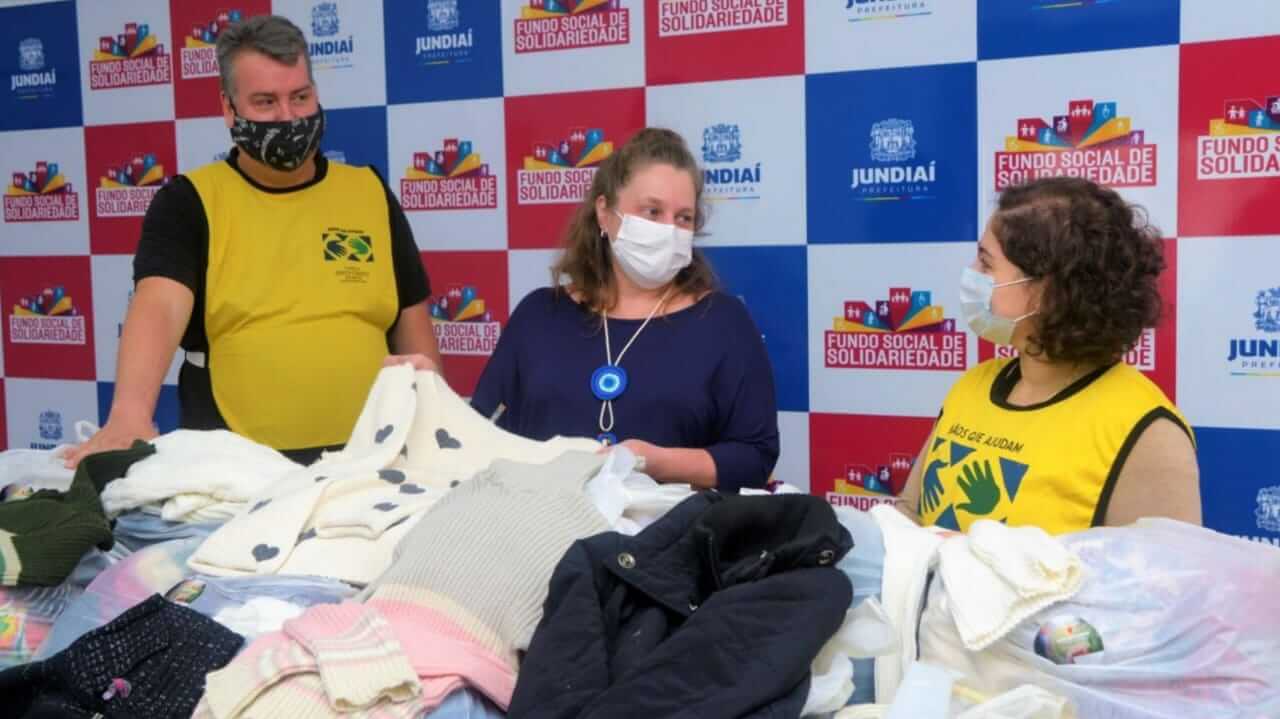 Um homem e duas mulheres em frente à doações de roupas do Fundo Social de Jundiaí