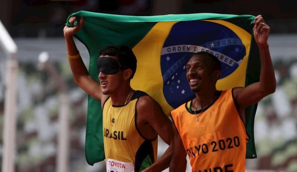 Atleta cego levanta bandeira do Brasil com treinador