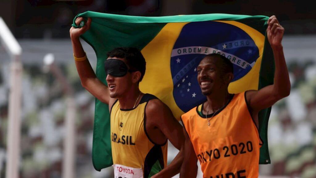 Atleta cego levanta bandeira do Brasil com treinador