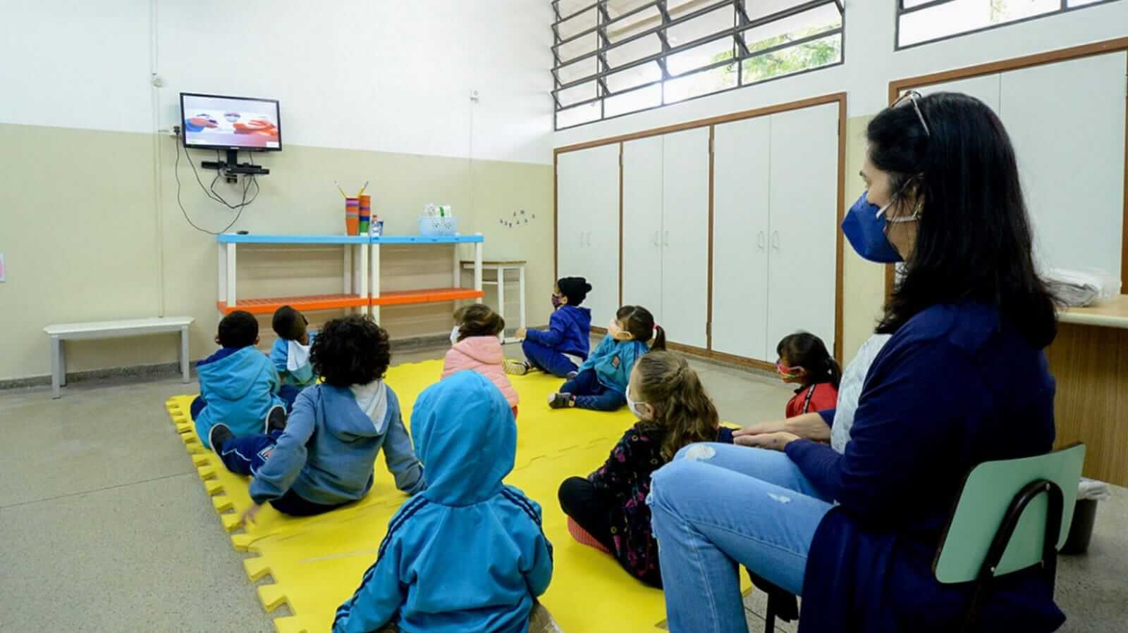 Crianças e professora em sala de aula assistindo vídeo em TV