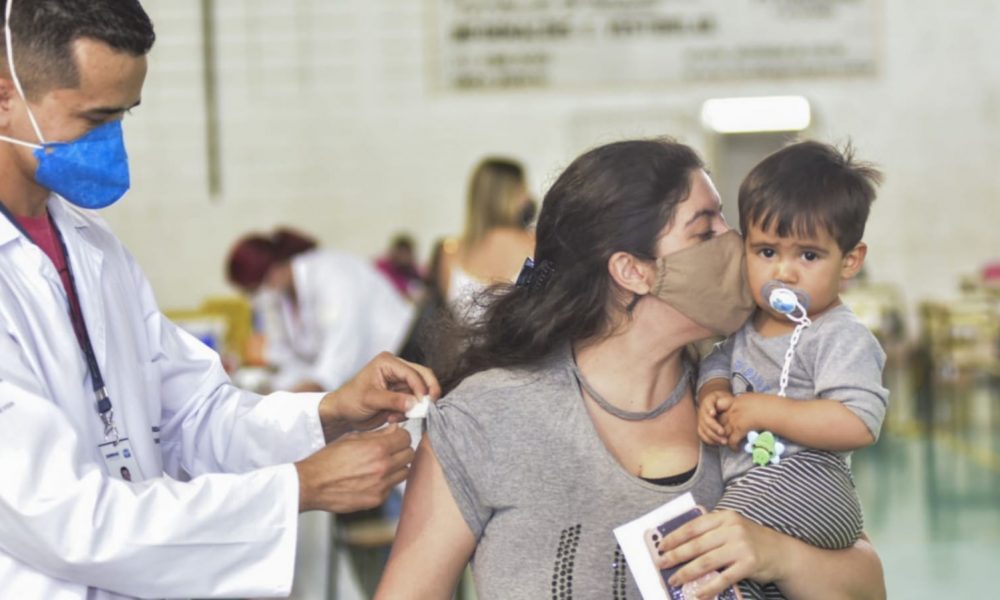 Mulher com bebê no colo, sendo vacinada em Jundiaí