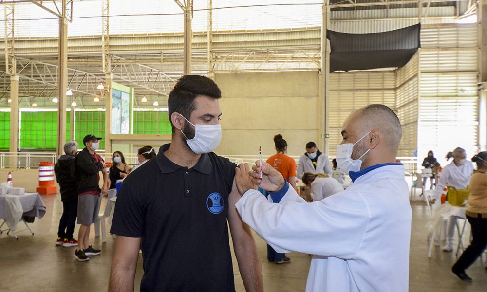 Homem sendo vacinado por um auxiliar da saúde