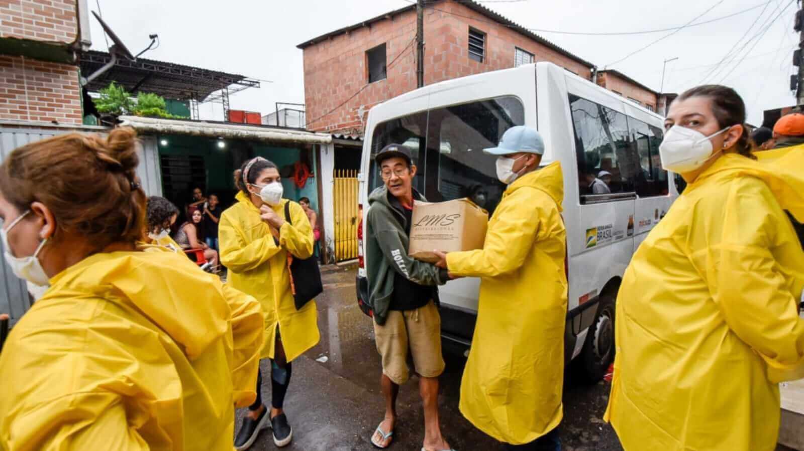 Pessoas com capas de chuva amarelas fazendo doações de alimentos
