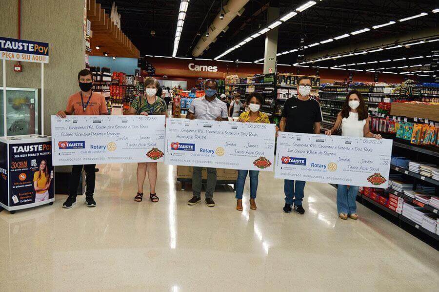 Representantes de entidades sociais, Tauste e Rotary Club Jundiaí segurando cheques gigantes