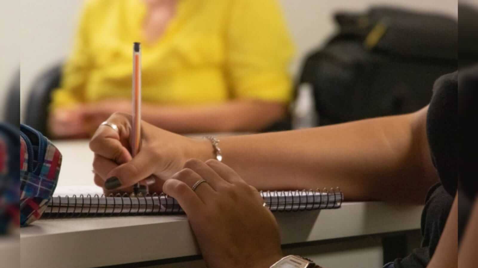 Pessoa com uma caneta na mão direita escrevendo em um caderno