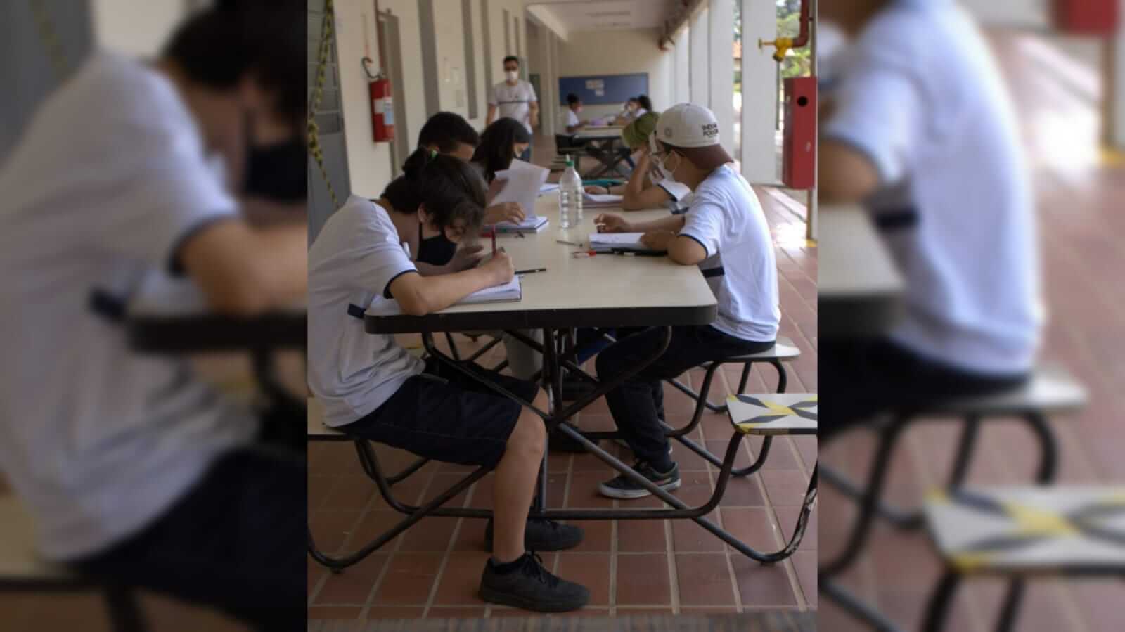 Adolescentes sentados envolta de uma mesa na escola estudando