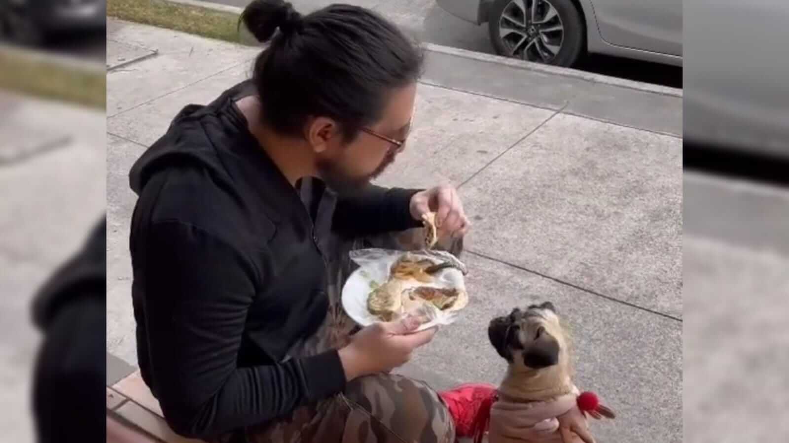 Homem comendo sentado no chão com cachorro pug