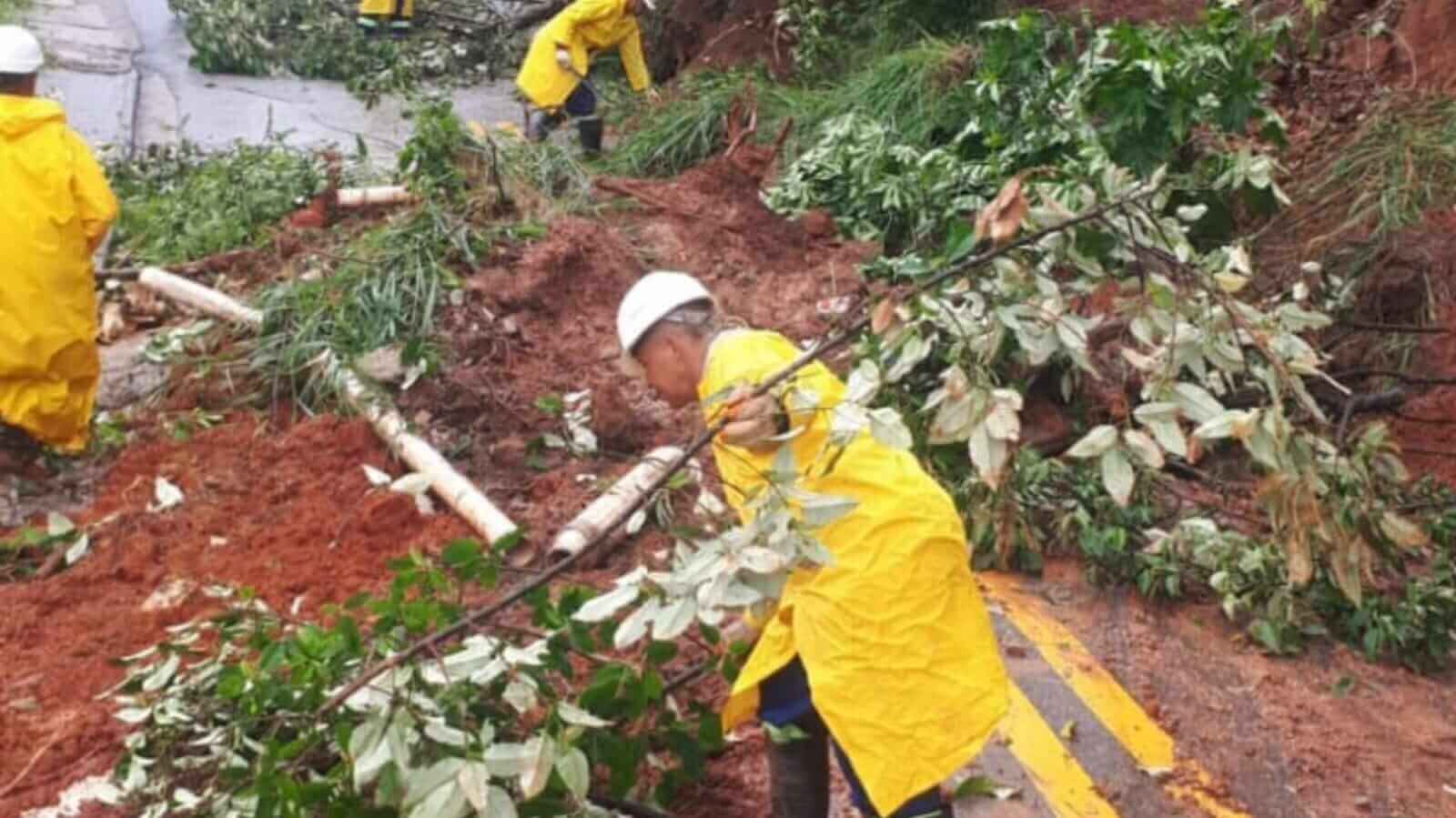 Trabalhadores de capa de chuva limpando rua com lama em Francisco Morato
