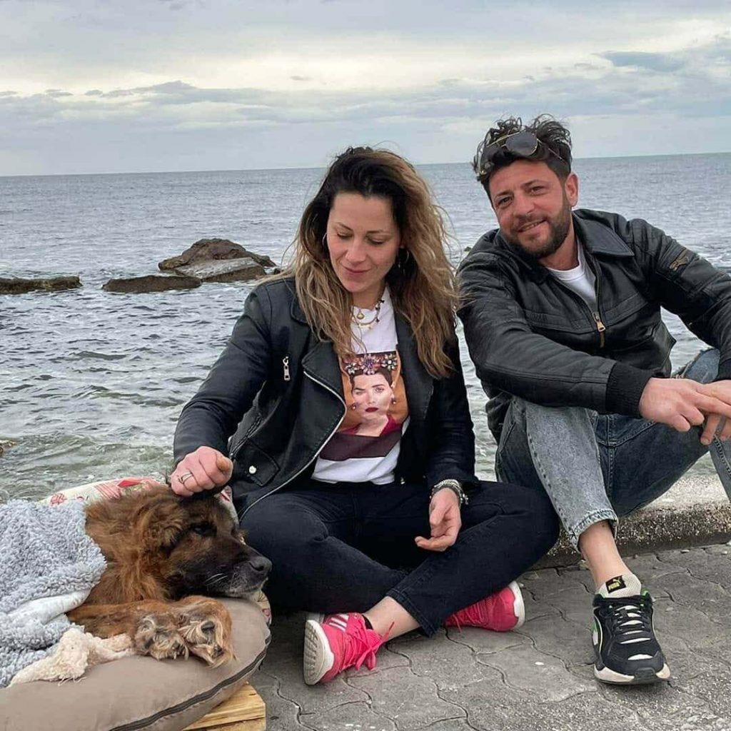 Cachorro deitado em colchão em frente ao mar com homem e mulher