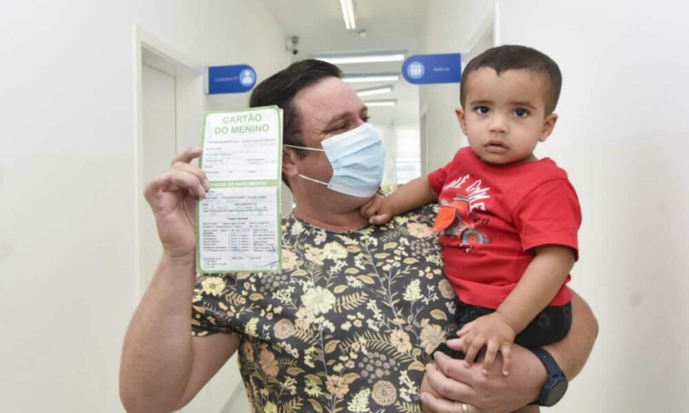 Pai com filho no colo mostrando carteirinha de vacinação