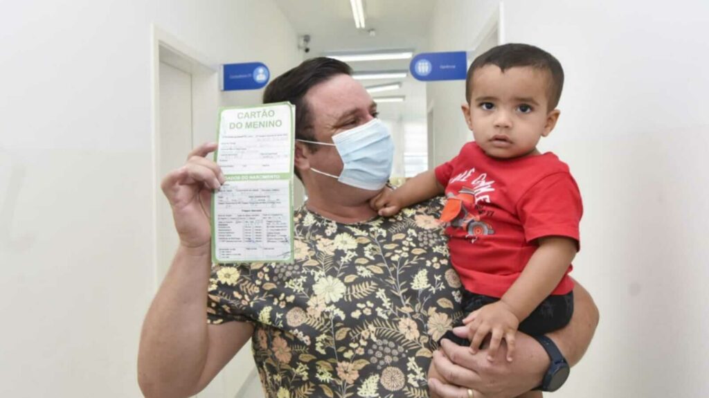 Pai com filho no colo mostrando carteirinha de vacinação