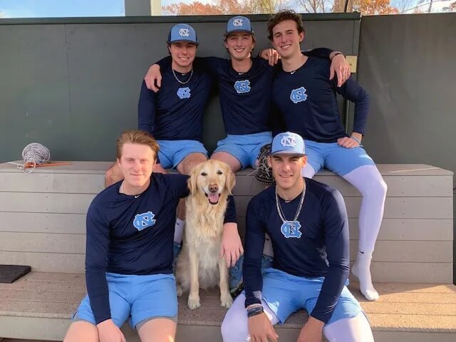 Five athletes pose for a photo with a golden retriever