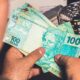 Pessoa segurando notas de R$ 100 reais brasileiros