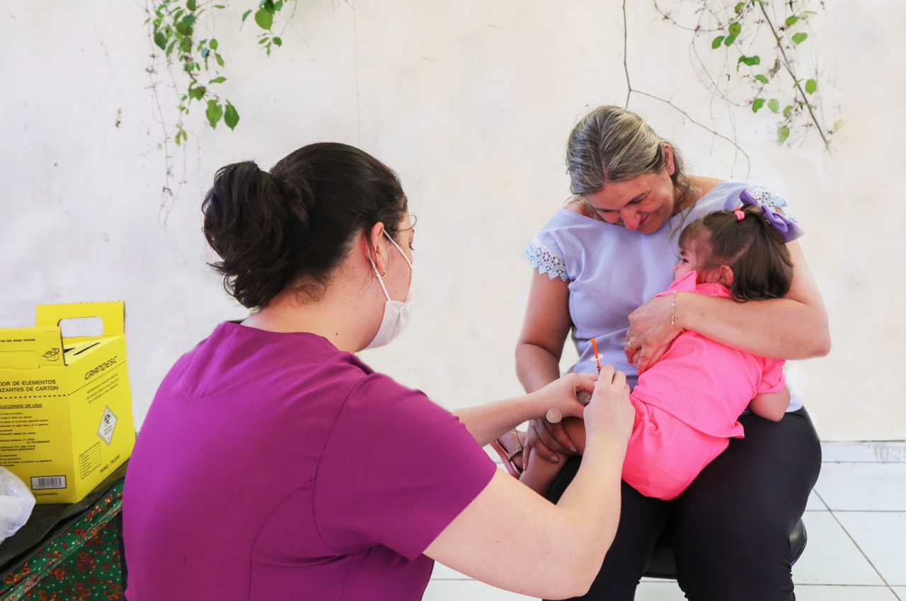 criança pequena no colo da mãe recebendo vacina no braço