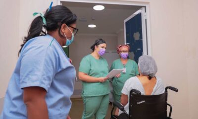 Paciente sentada em uma cadeira de rodas, ao lado de 3 enfermeiras, sendo levada para o centro cirúrgico