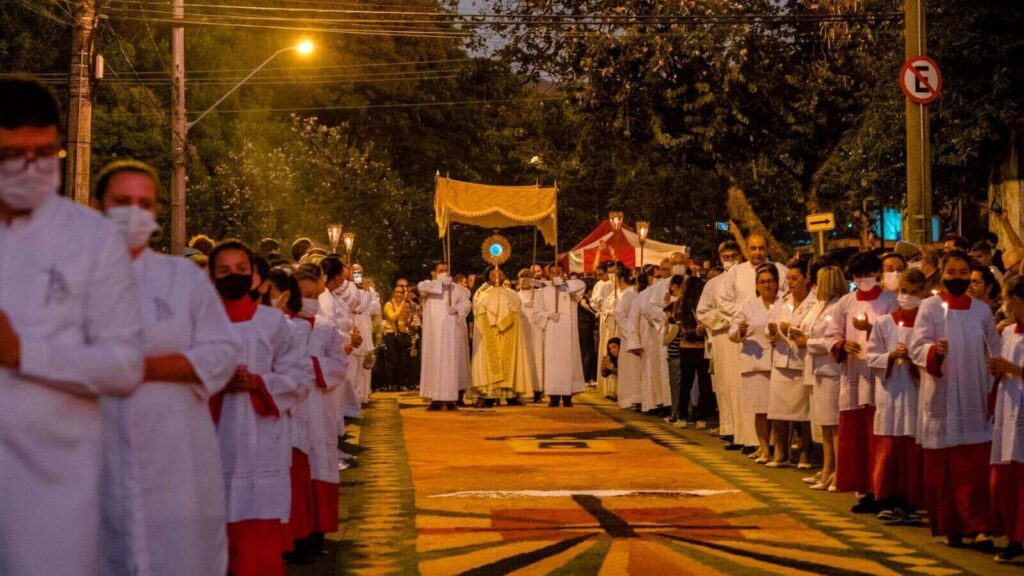 Procissão de Corpus Christi em Jundiaí com tapetes coloridos e grande número de fiéis, à noite.