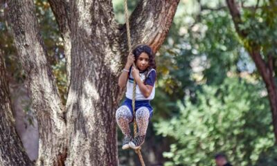 Criança brincando em uma corda pendurada em árvore durante atividade ao ar livre em escola, destacando diversão e natureza.