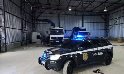 Galpão com caminhões desmontados e viatura da Polícia Civil com luzes ligadas em primeiro plano