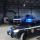 Galpão com caminhões desmontados e viatura da Polícia Civil com luzes ligadas em primeiro plano