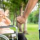 Imagem mostra uma idosa em cadeira de rodas sendo ameaçada por um homem com punho fechado em um parque, simbolizando violência contra idosos.
