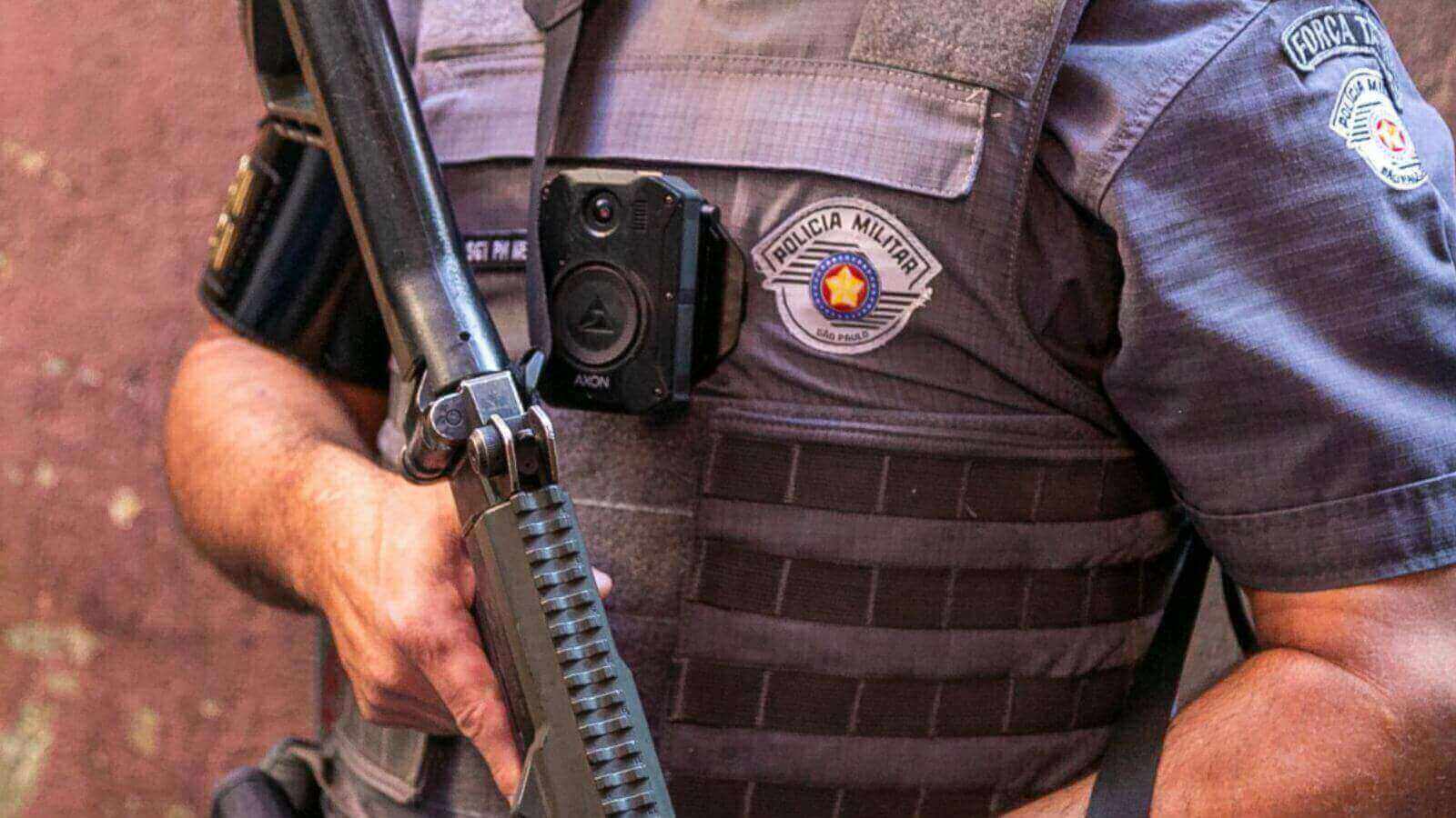 Policial Militar do Estado de São Paulo com arma nas mãos e câmera corporal no peito.