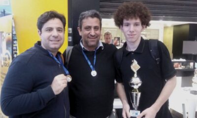 Três homens do Time Jundiaí de Xadrez posando com medalhas e um troféu, celebrando uma conquista em um ambiente de competição.