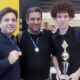 Três homens do Time Jundiaí de Xadrez posando com medalhas e um troféu, celebrando uma conquista em um ambiente de competição.