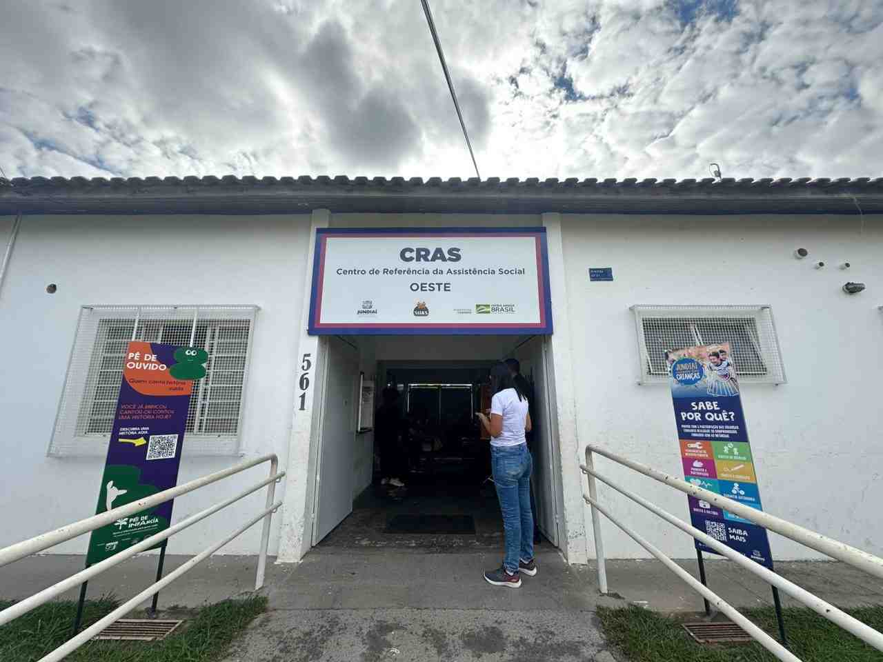 Centro de Referência da Assistência Social (CRAS) Oeste em Jundiaí, mostrando entrada principal com banners informativos e uma pessoa na porta.