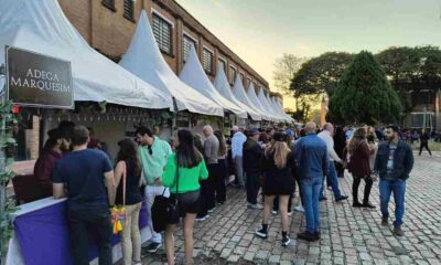 Pessoas visitam barracas de vinícolas no evento "Dia do Vinho" em Jundiaí, em um ambiente ao ar livre com céu claro.