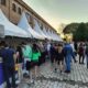 Pessoas visitam barracas de vinícolas no evento "Dia do Vinho" em Jundiaí, em um ambiente ao ar livre com céu claro.