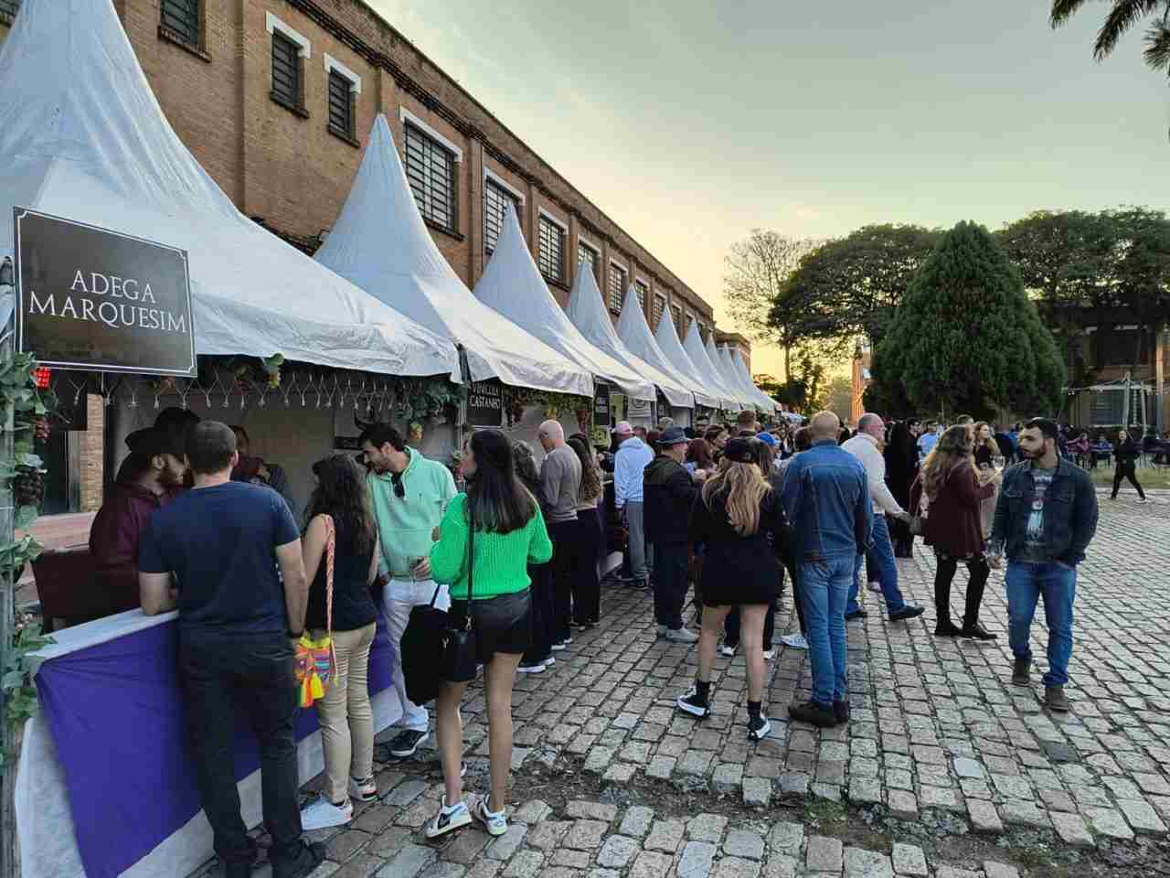 Pessoas visitam barracas de vinícolas no evento "Dia do Vinho" em Jundiaí, em um ambiente ao ar livre com céu claro.