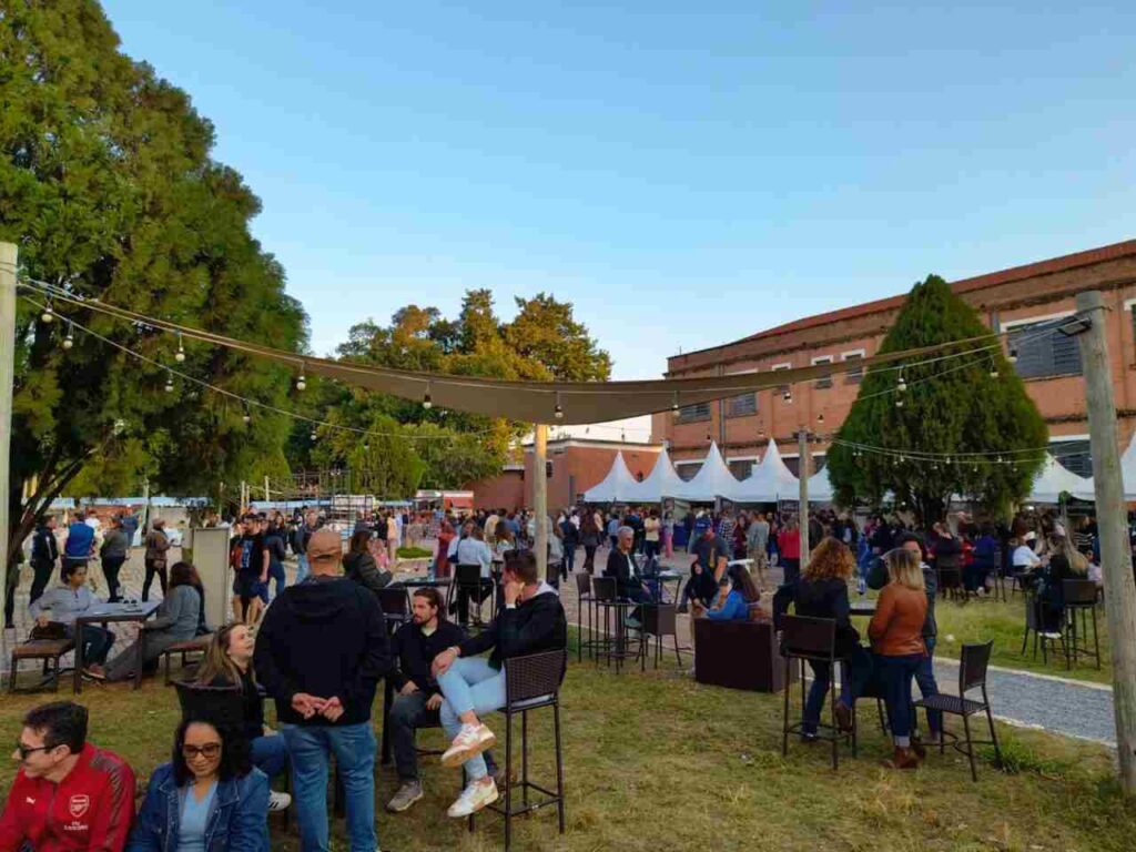 Público aproveita o evento "Dia do Vinho" em Jundiaí, com várias pessoas sentadas e em pé em um espaço ao ar livre com barracas ao fundo.
